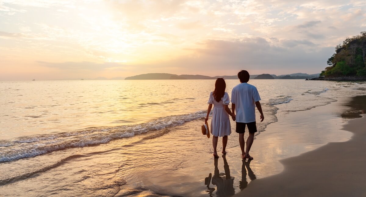 Couple walks along beach at sunrise after adjustment of status through marriage